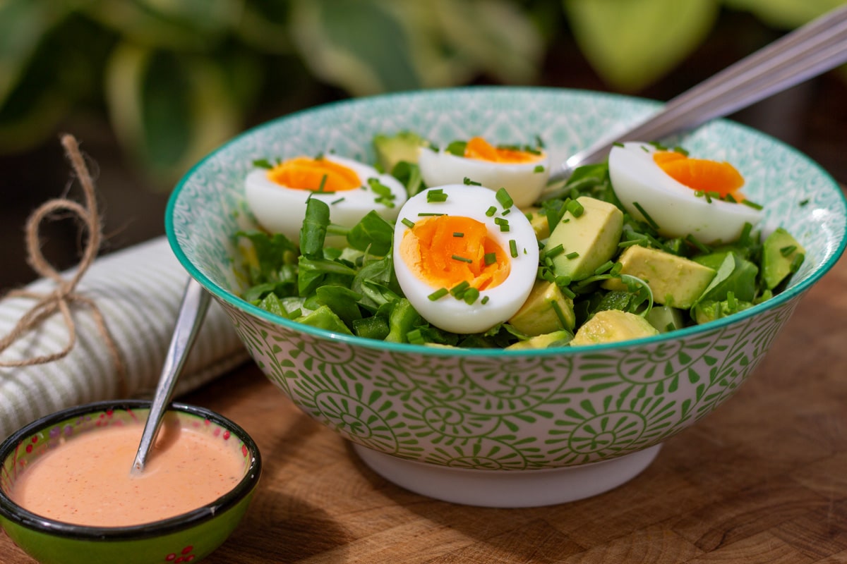 Avocadosalat med æg og lime-srirachadressing pyntet med purløg
