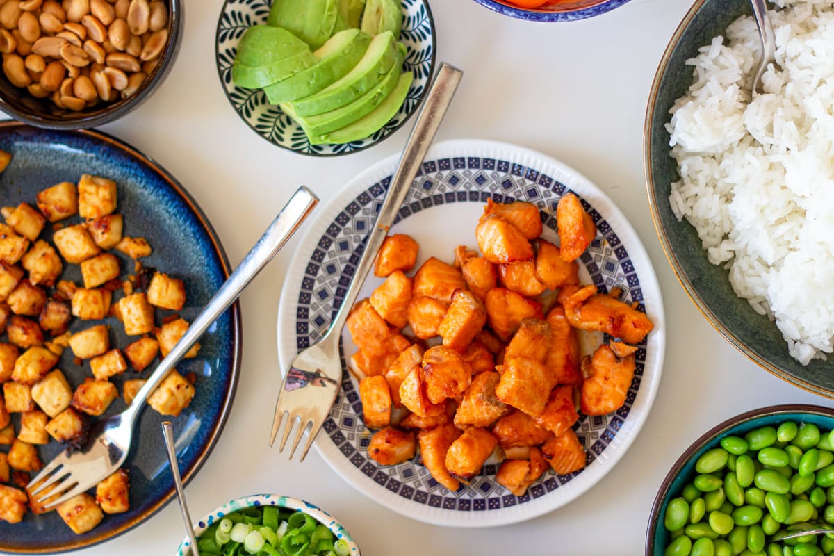 Bord anrettet med ingredienser til poke bowl: marineret laks bagt i aifrryer, avocado, ris og peanuts.