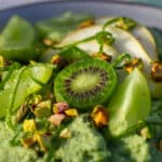 Lysegrøn energigrød pyntet med kiwibær, grønne dryer, pære, limeskal og pistcienødder