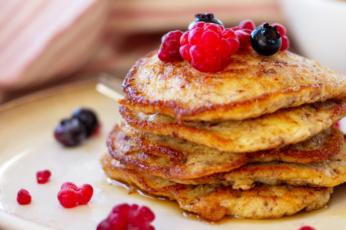 En lille stabel pandekager af mandelmel med sirup, hindbær og blåbær.