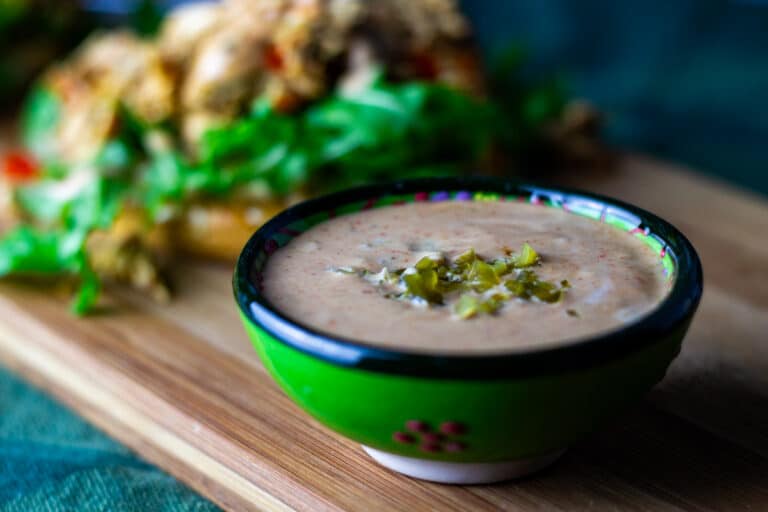 Dressing med syltede jalapenos og paprika foran en burger.