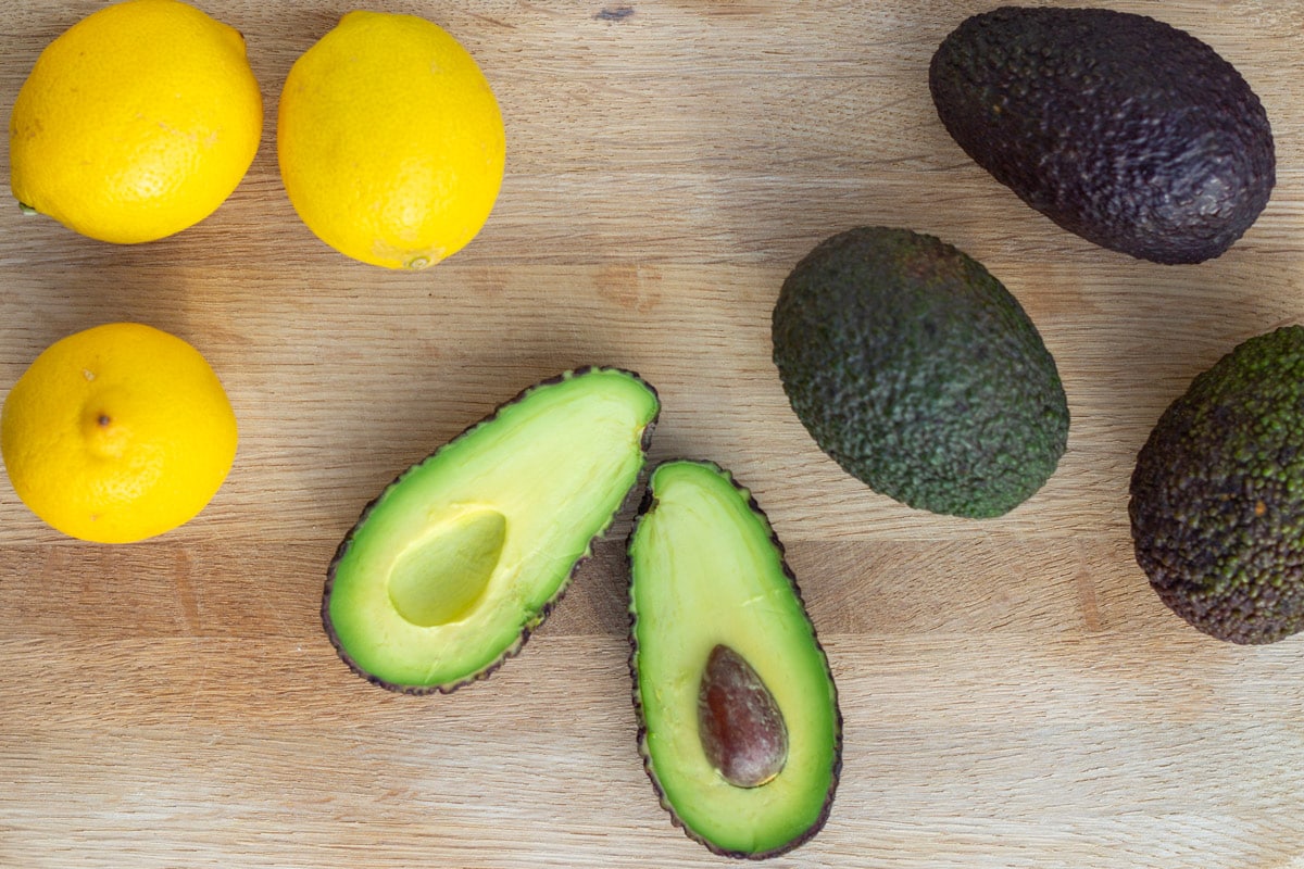 Avocado skåret over i halve og hele avocadoer på et skærebræt