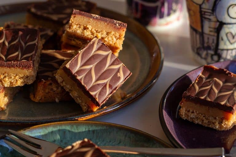 Karamelsnitter med glutenfri bund af mandler og kokos, karamel og chokolade anrettet på tallerken.