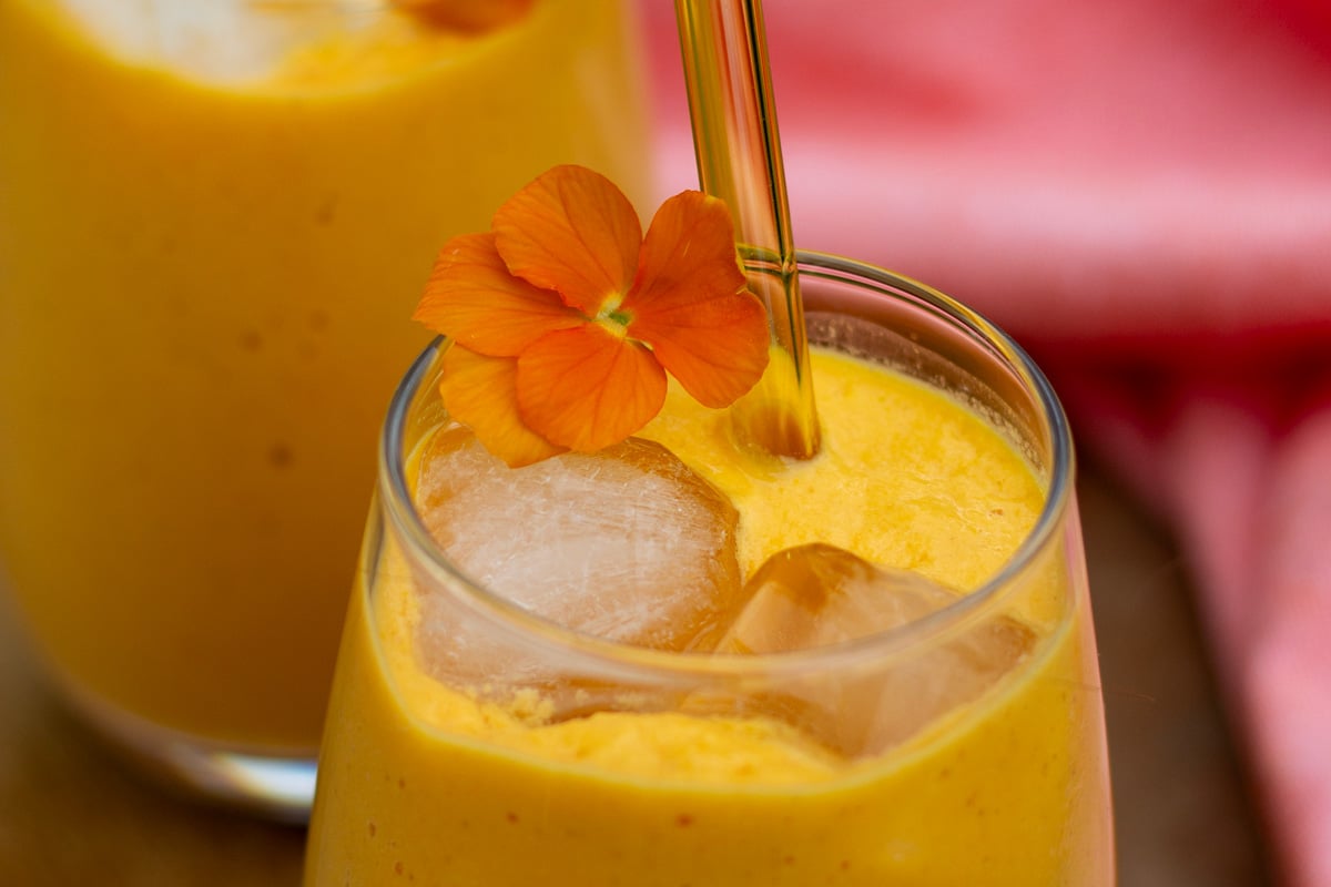 Gul energismoothie med gulerod, appelsin, peberfrugt og kefir pyntet med orange stedmoderblomser